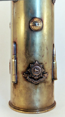 Shell with badges as the Worcestershire Regiment, cartridges soldered, and small flaming bombs